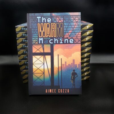 A book titled "The Warm Machine" in hardcover, leaned up against a stack of them. The front cover features a silhouette of a robot looking at the sunrise/sunset.
